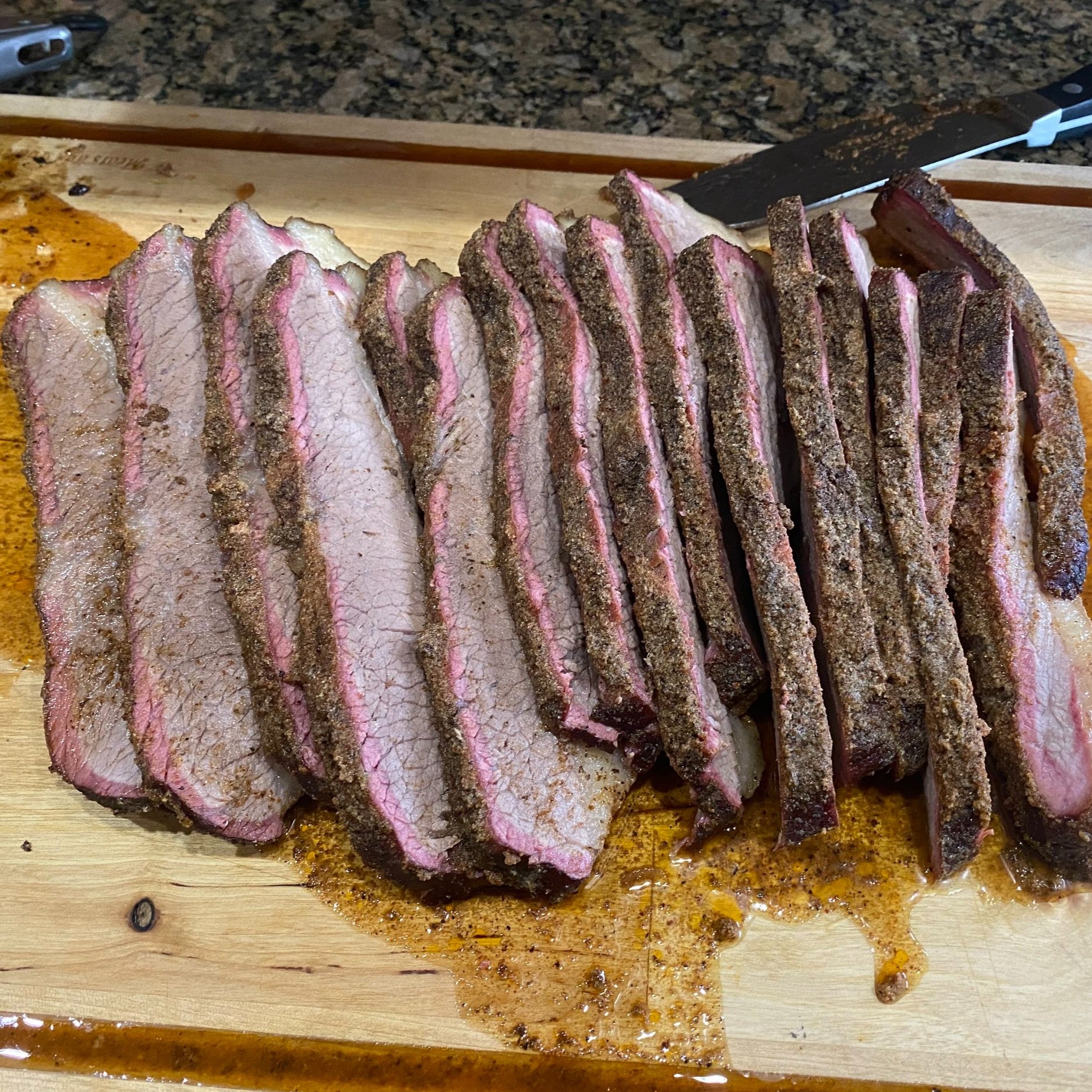 Sliced smoked brisket on a wooden cutting board, showcasing tender pink meat with a flavorful bark, surrounded by juices.